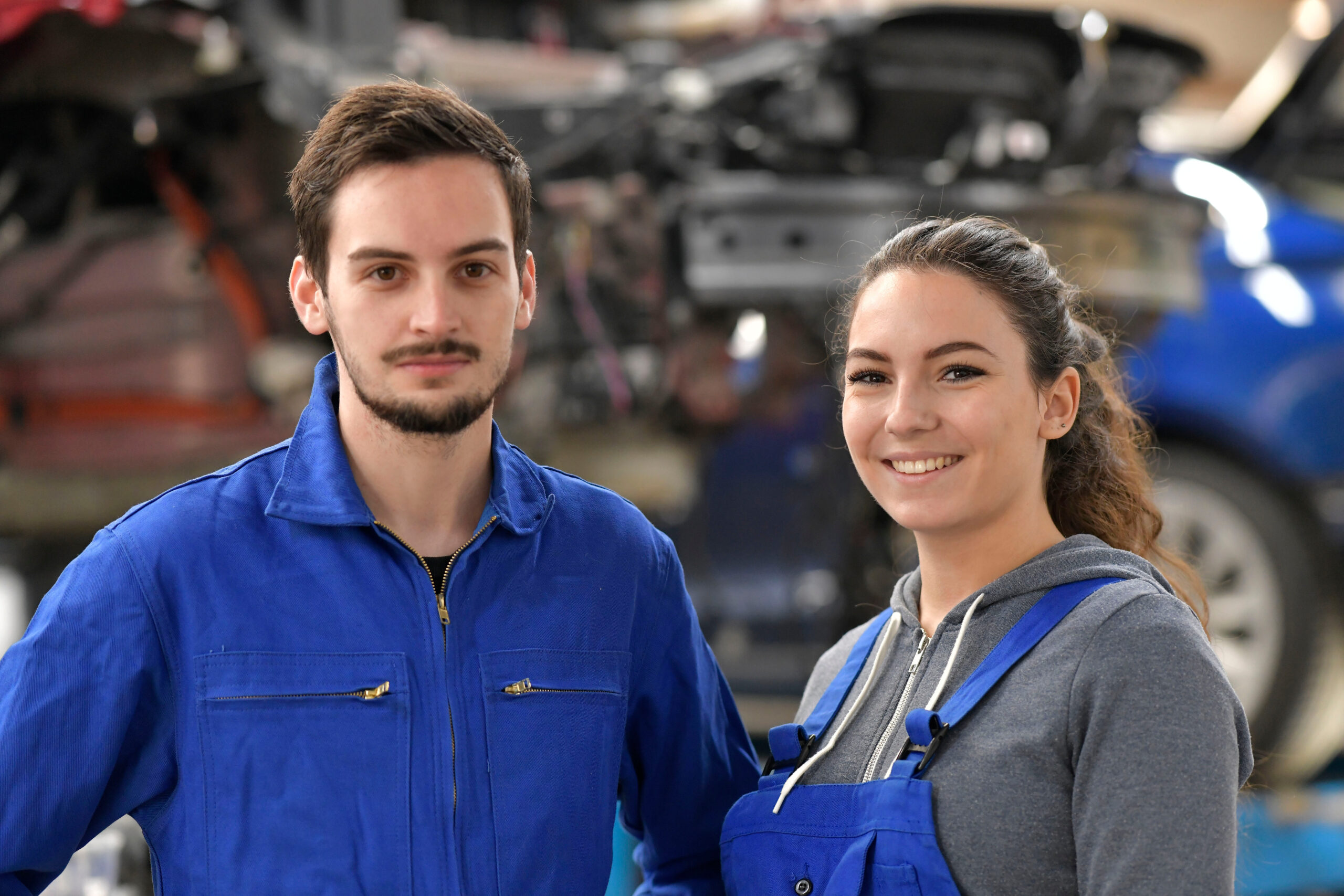 Zwei junge Fachkräfte in blauer Arbeitskleidung in einer Werkstatt